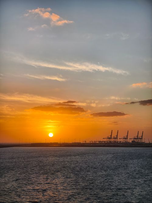 Free Vibrant sunset over a harbor with silhouetted cranes against an orange sky. Stock Photo