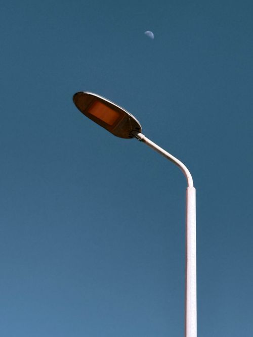 Free Minimalist photograph of a street lamp with a crescent moon in the clear blue sky. Stock Photo