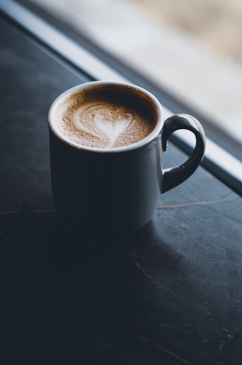 Free A stylish cup of coffee with latte art sits on a sleek marble table near a window. Stock Photo