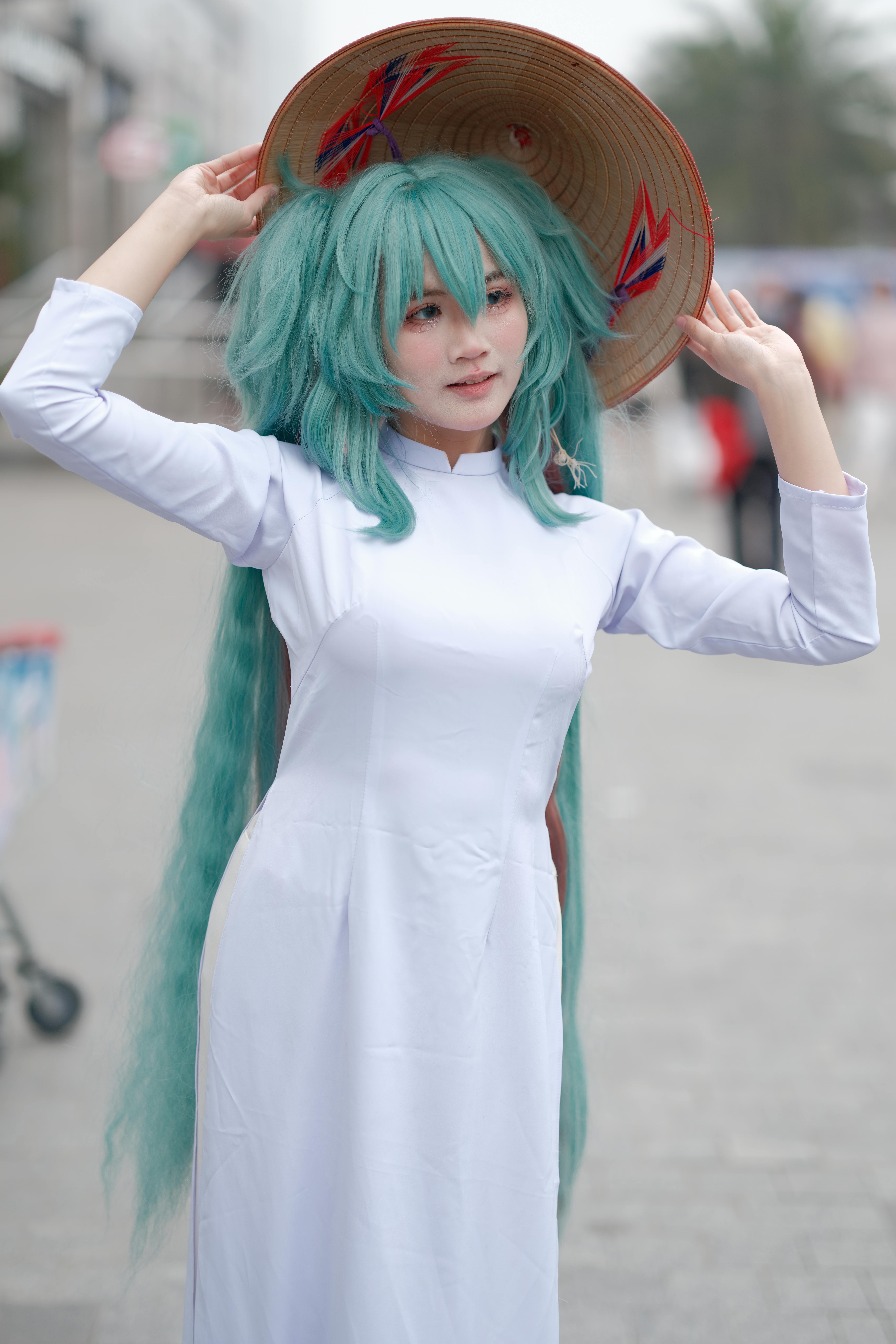 A woman in cosplay wearing a traditional Vietnamese Ao Dai and straw hat outdoors.