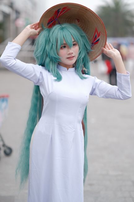 A woman in cosplay wearing a traditional Vietnamese Ao Dai and straw hat outdoors.