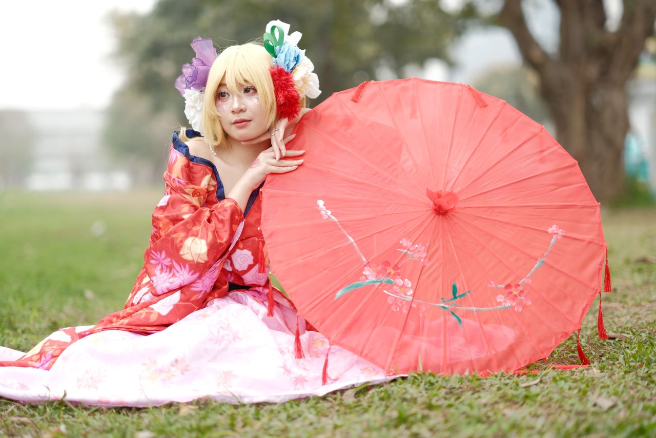 a woman in a colorful kimono sits on grass holding a parasol set in a