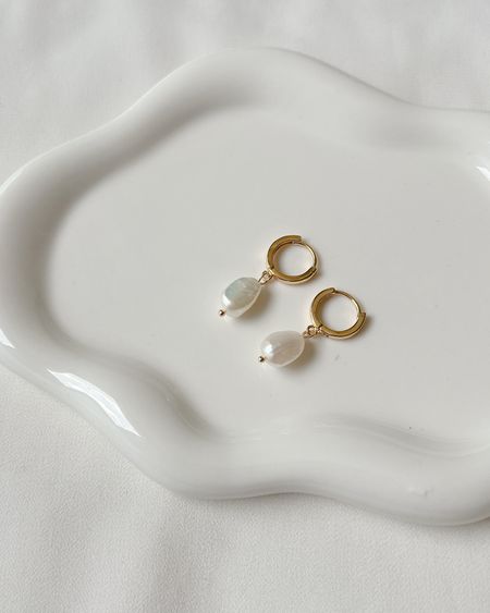 Small gold huggie hoop earrings with pearl drops on a white ceramic dish