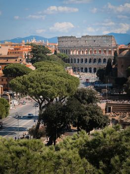 Aerial shot of the iconic Colosseum in Rome, Italy, surrounded by lush greenery under a bright sky.