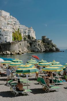 Tourists relaxing under umbrellas on a sunny day at the beach in Amalfi, Italy.