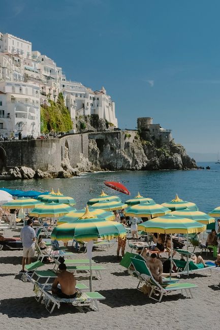 Tourists relaxing under umbrellas on a sunny day at the beach in Amalfi, Italy.