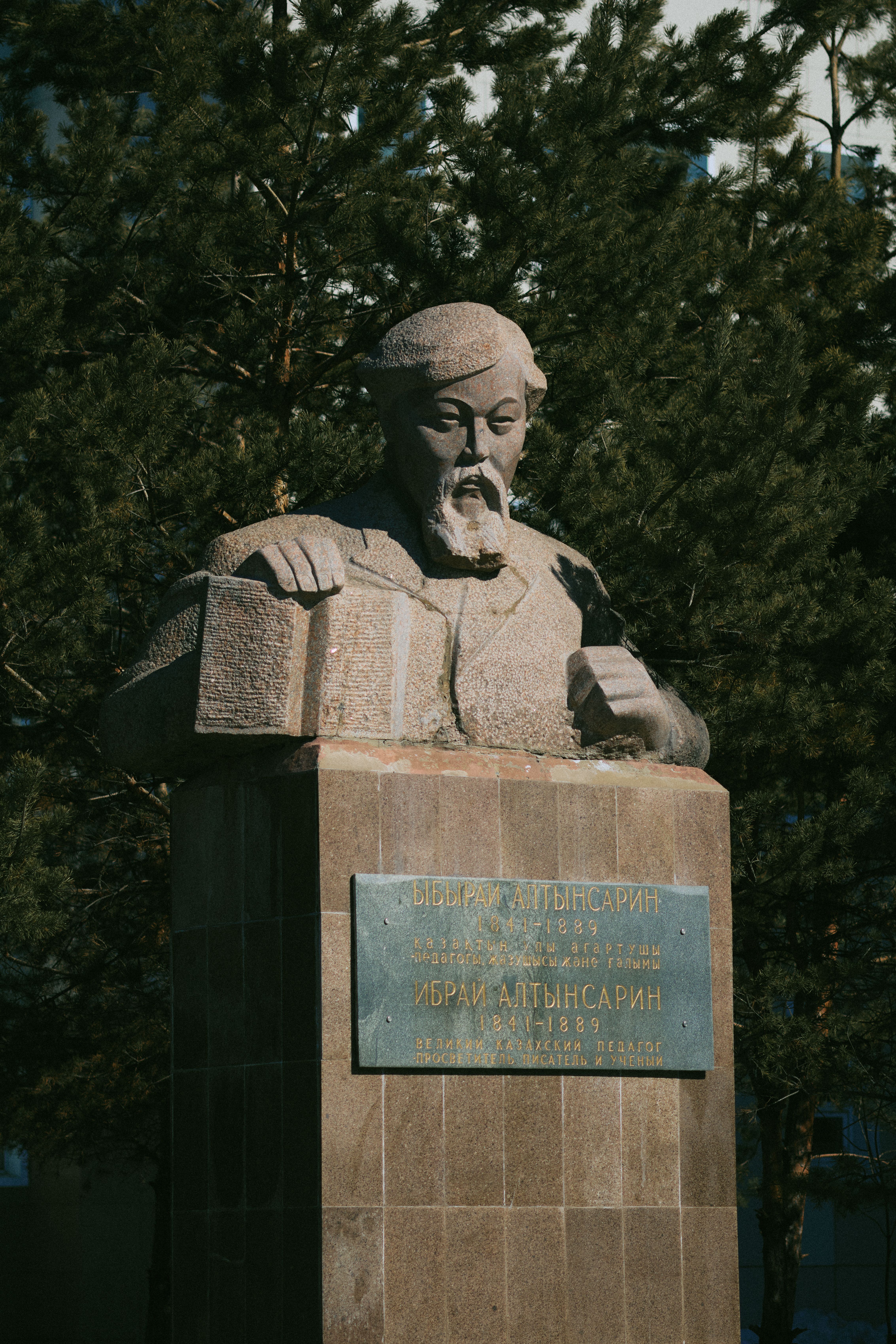 Stone statue of a historical figure set against trees, under sunlight, offering cultural insight.