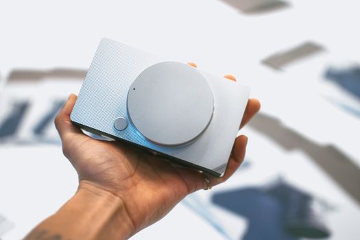 Close-up of a hand holding a sleek gray portable speaker against a blurred background.