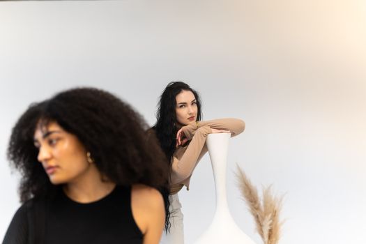 Artistic studio portrait of two diverse women with modern decor. Stylish and contemplative.