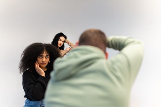 Two models pose during a photo shoot with a photographer in a studio setting.