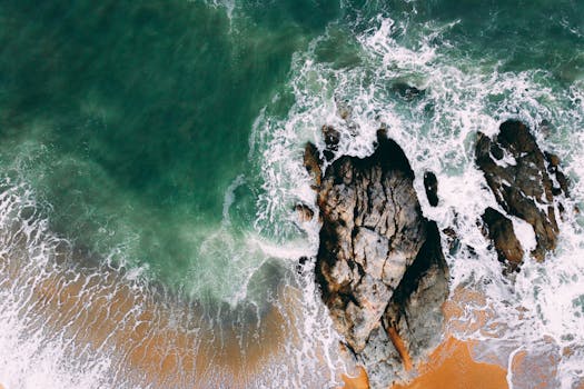 Drone shot capturing waves crashing on a rocky seashore with vibrant ocean colors.