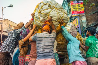 A group of people working together to load a large bundle onto a cart