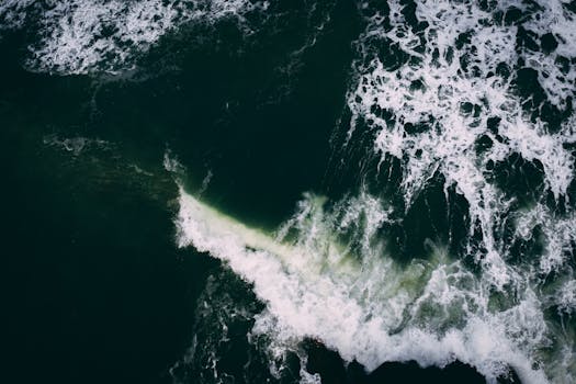 A breathtaking aerial view of ocean waves crashing and creating seafoam in deep green waters.