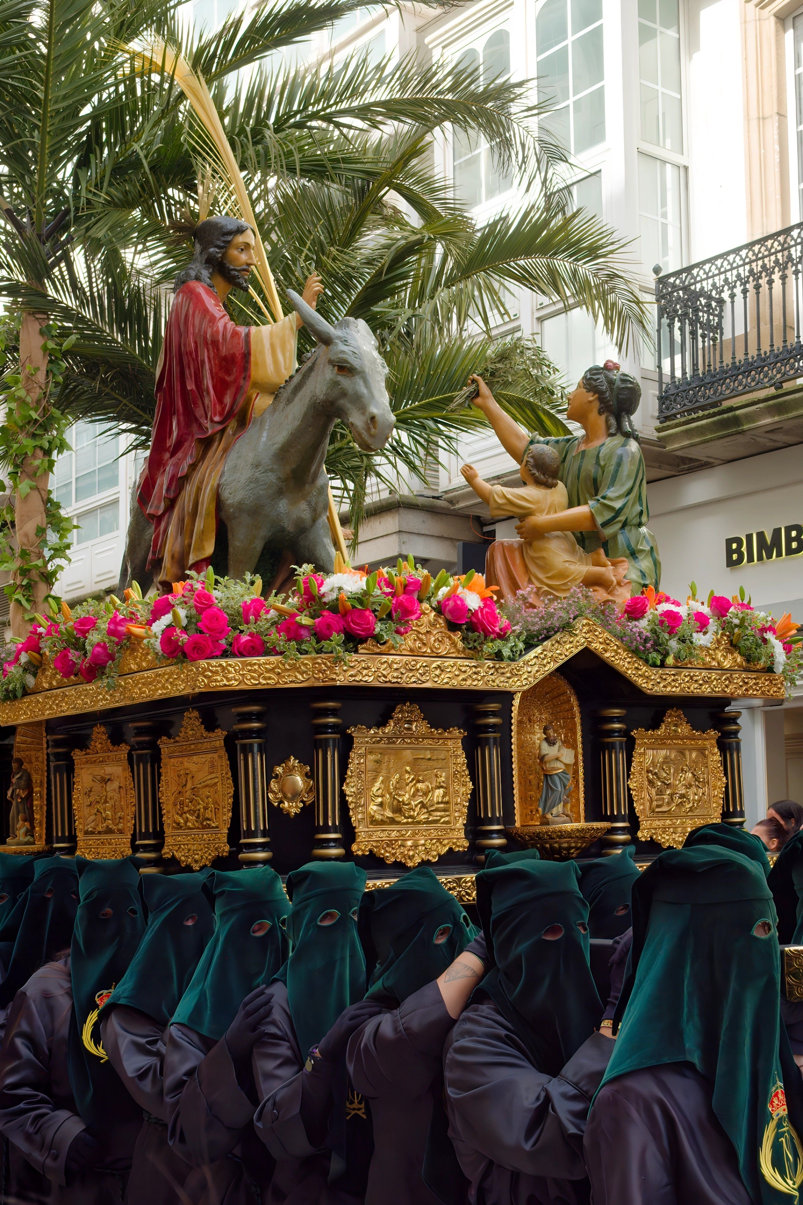 Colorful Semana Santa procession featuring a religious statue on a decorated platform in Ferrol, Spain.