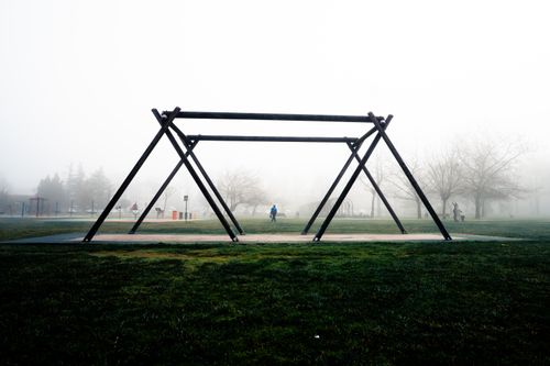 Free A misty park with a large empty swing frame and people in the distance. Stock Photo