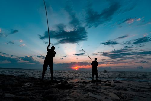 Free Two fishermen silhouetted against a vibrant sunset sky over the Black Sea, casting fishing rods. Stock Photo