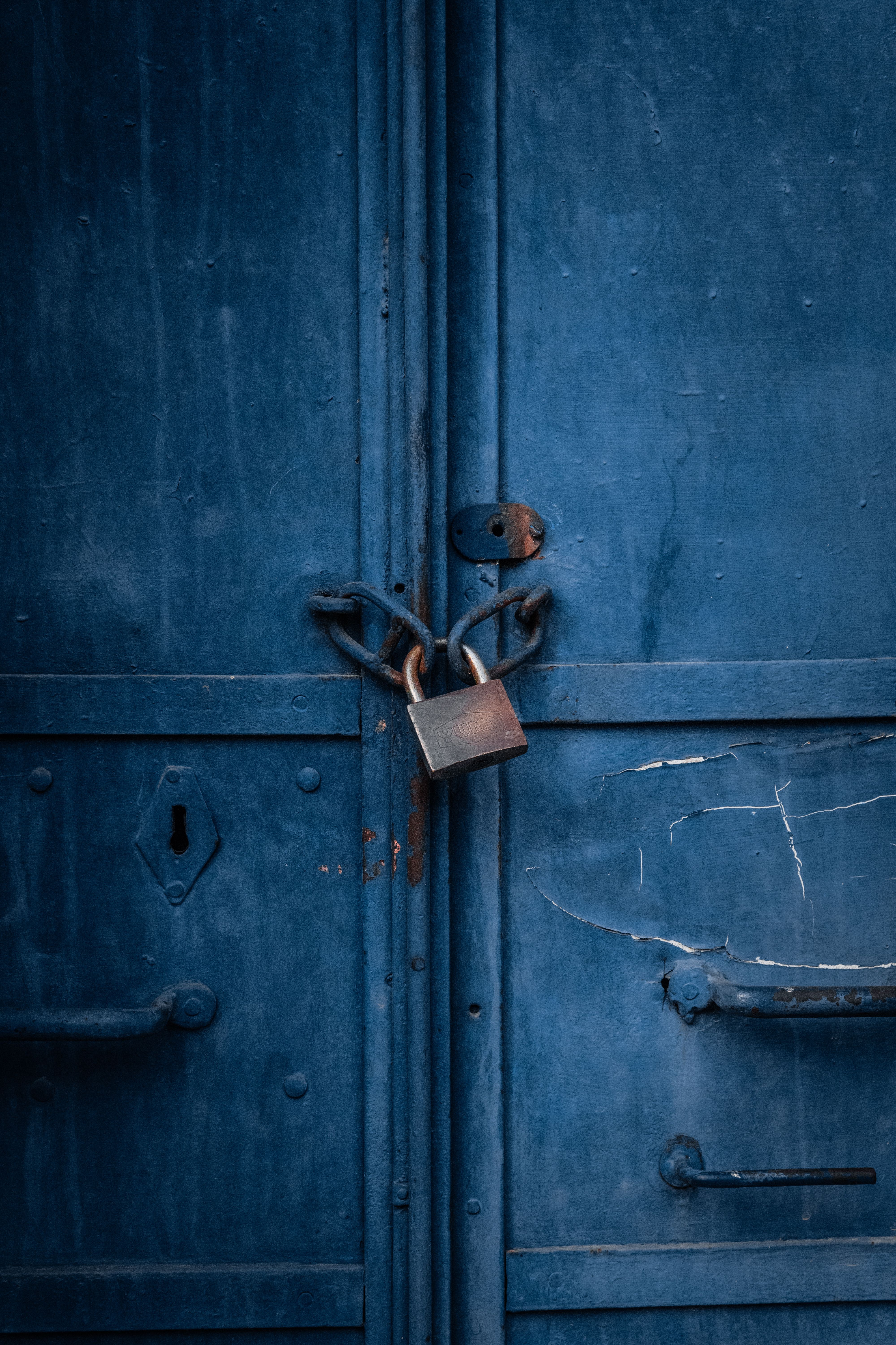 Close-up of a blue metal door with a rusty padlock, symbolizing security.