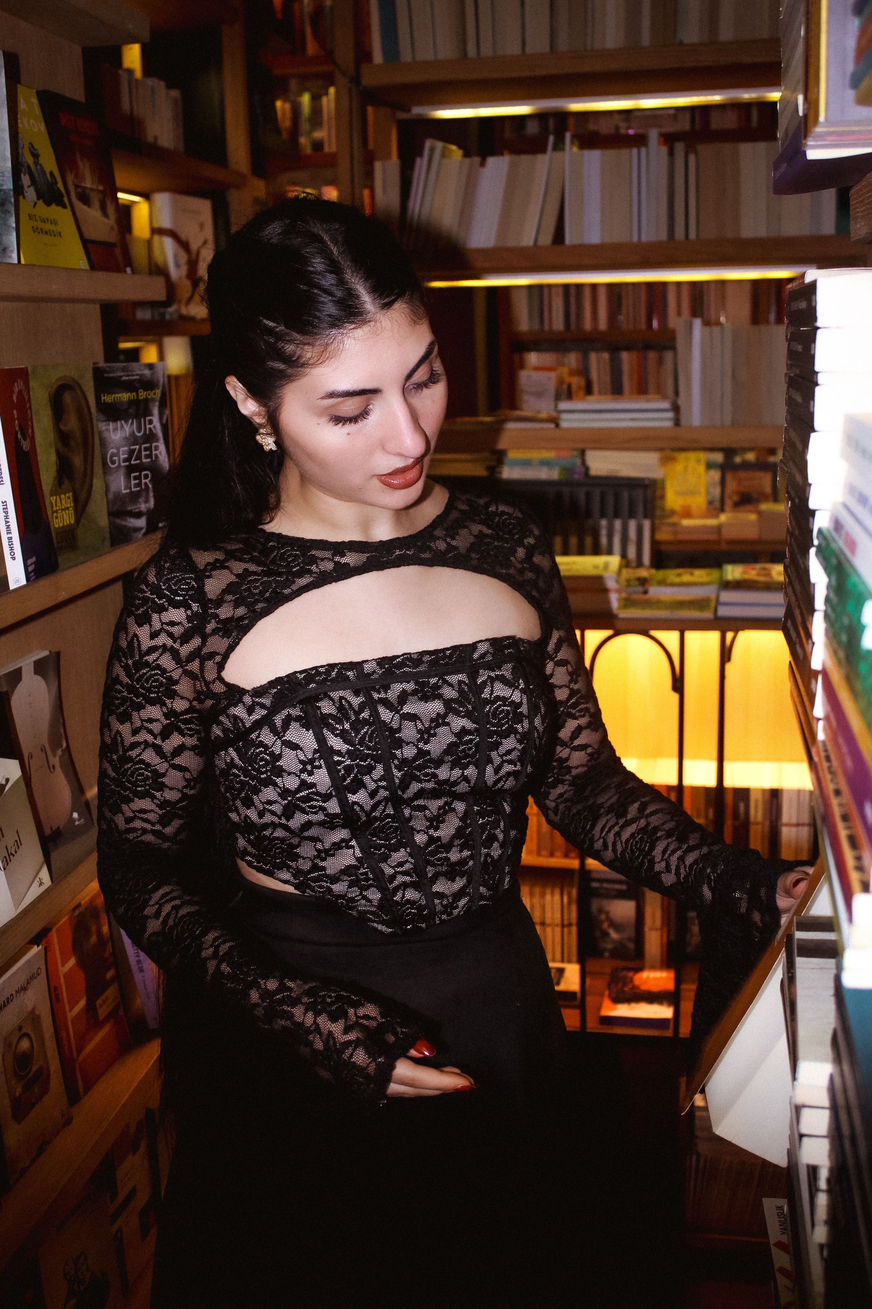 Elegant woman wearing lace dress while browsing books in a cozy, well-lit bookstore.