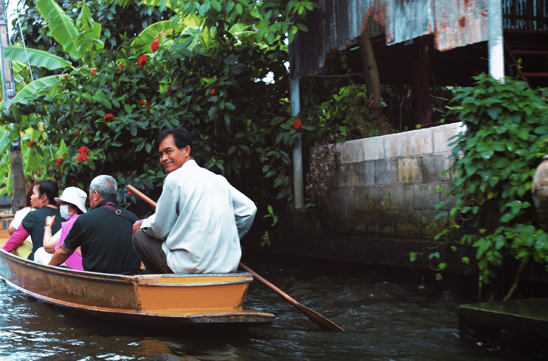 Travelers and their boat guide exploring a Bangkok canal by traditional wooden boat
