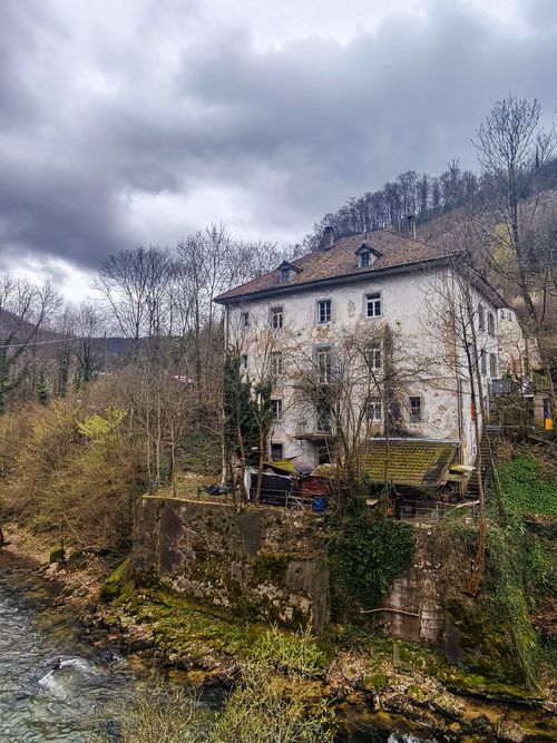 Free A rustic riverside house surrounded by leafless trees and cloudy sky. Stock Photo