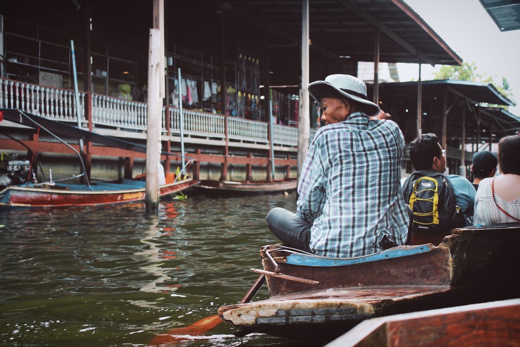 Travelers moving by wooden boat among vendors at a Bangkok floating market