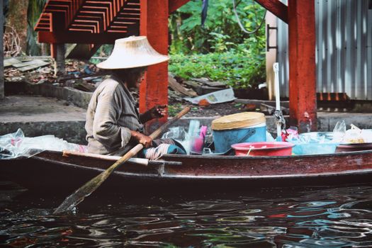 A local vendor paddles a boat selling goods on a canal in Bangkok, Thailand, showcasing Thai culture and lifestyle.