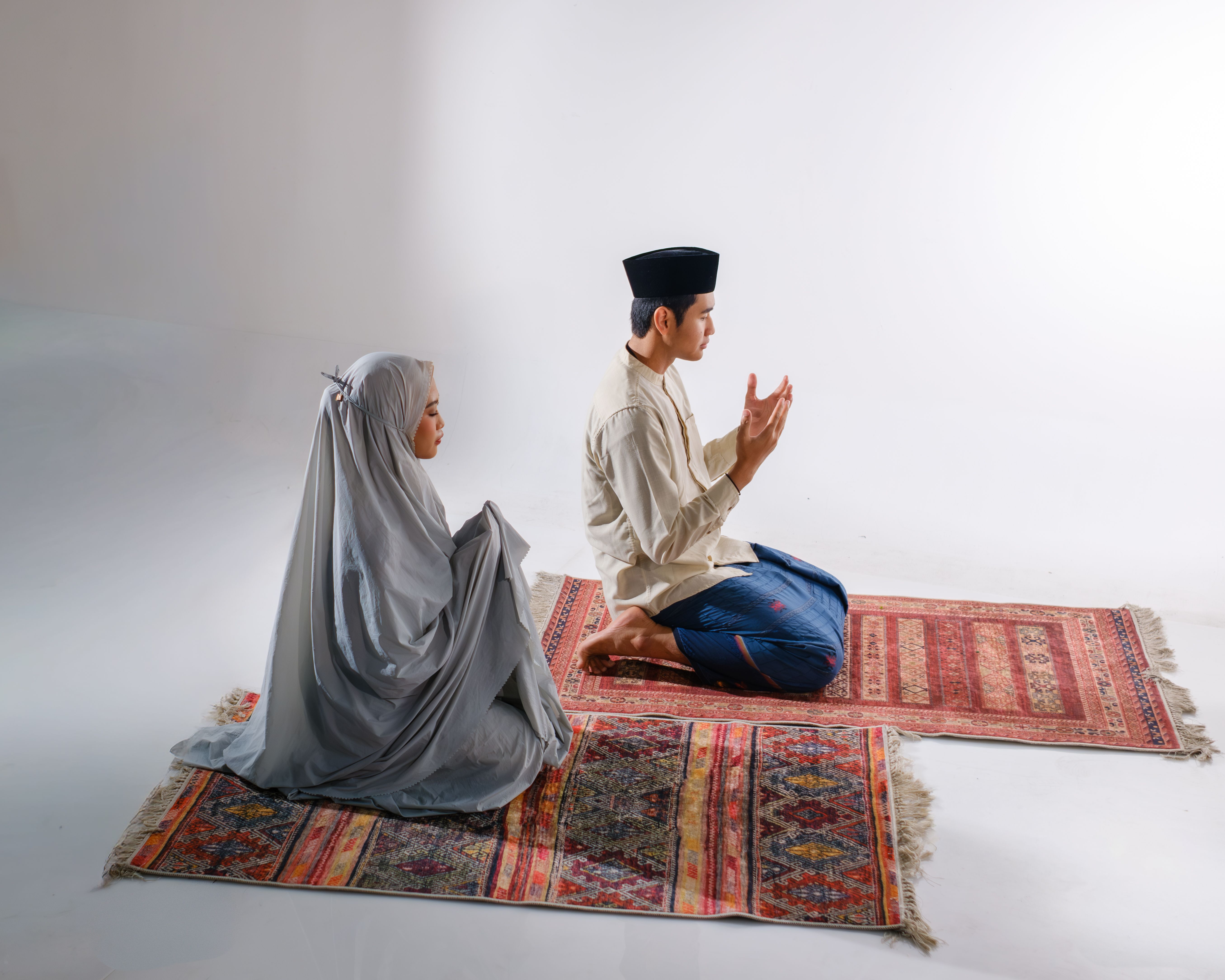 A Muslim couple performs prayer on traditional mats, highlighting spirituality and cultural heritage.