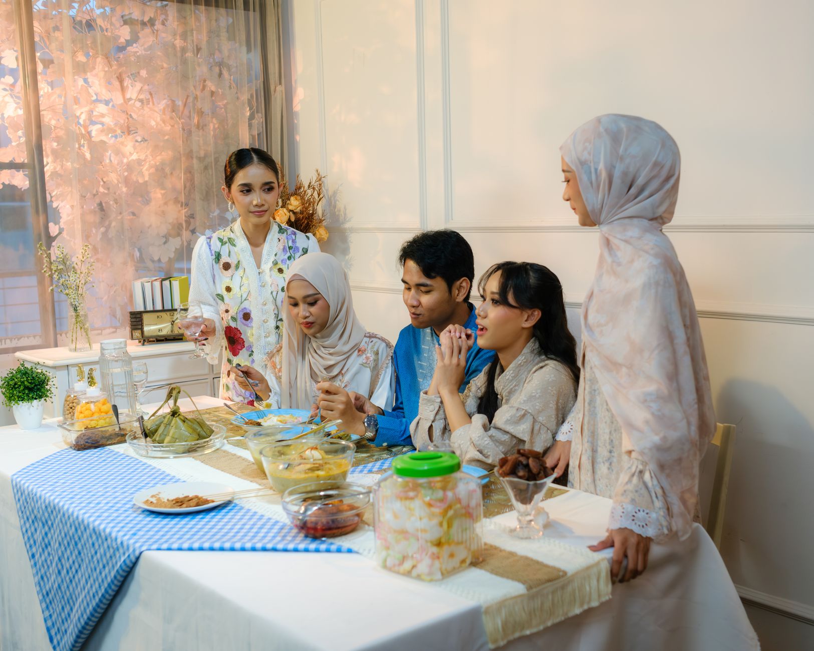 A family gathers indoors for a festive Eid meal in Jakarta, Indonesia, showcasing traditional attire and dishes.