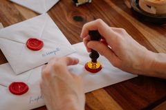 Close-up of person applying red wax seals to envelopes on a wooden table, showcasing traditional letter sealing.