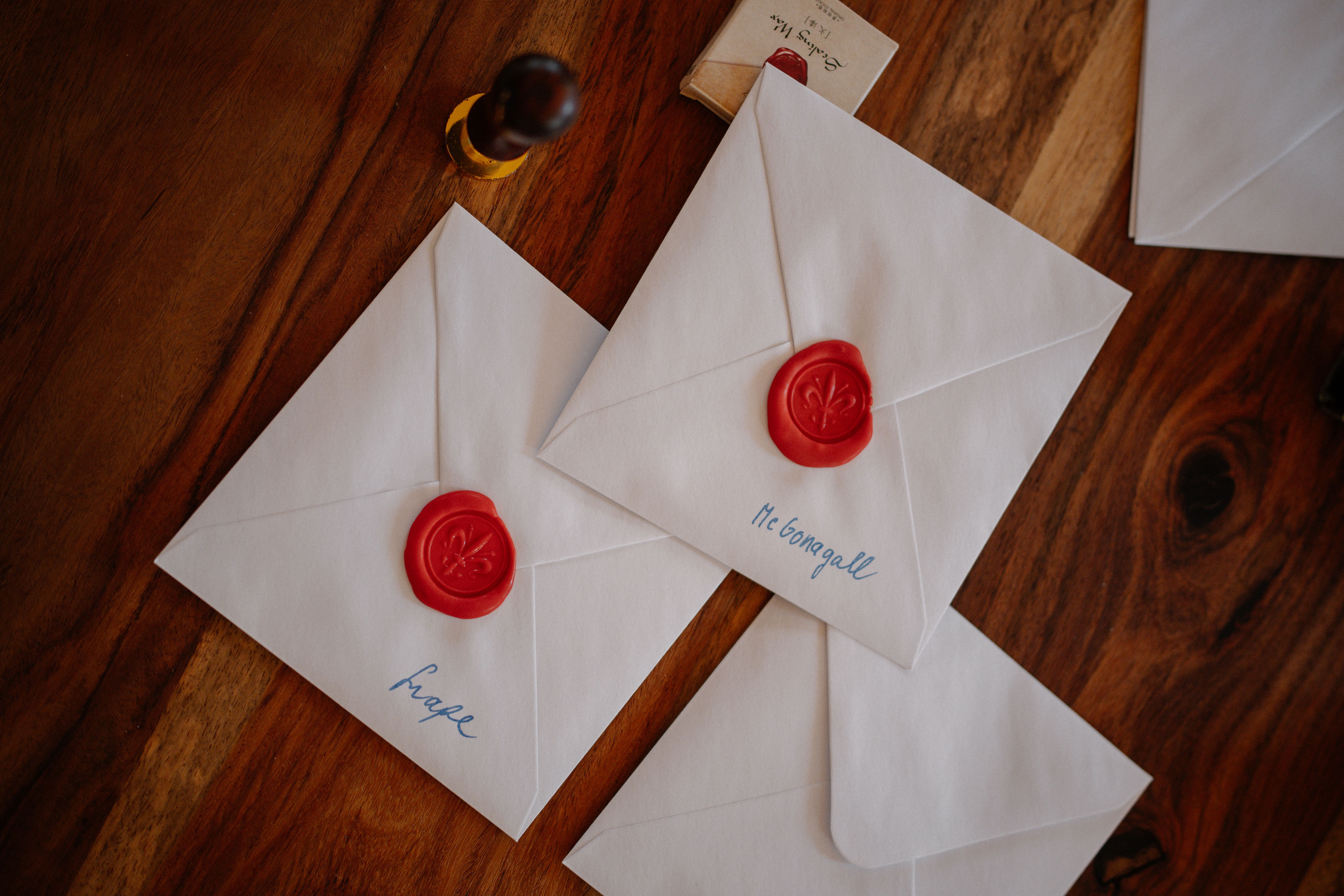 Three white envelopes sealed with red wax are creatively displayed on a wooden table, suggesting a vintage theme.