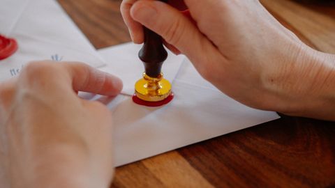 A person sealing an envelope with a wax stamp on a wooden table, creating a vintage feel.