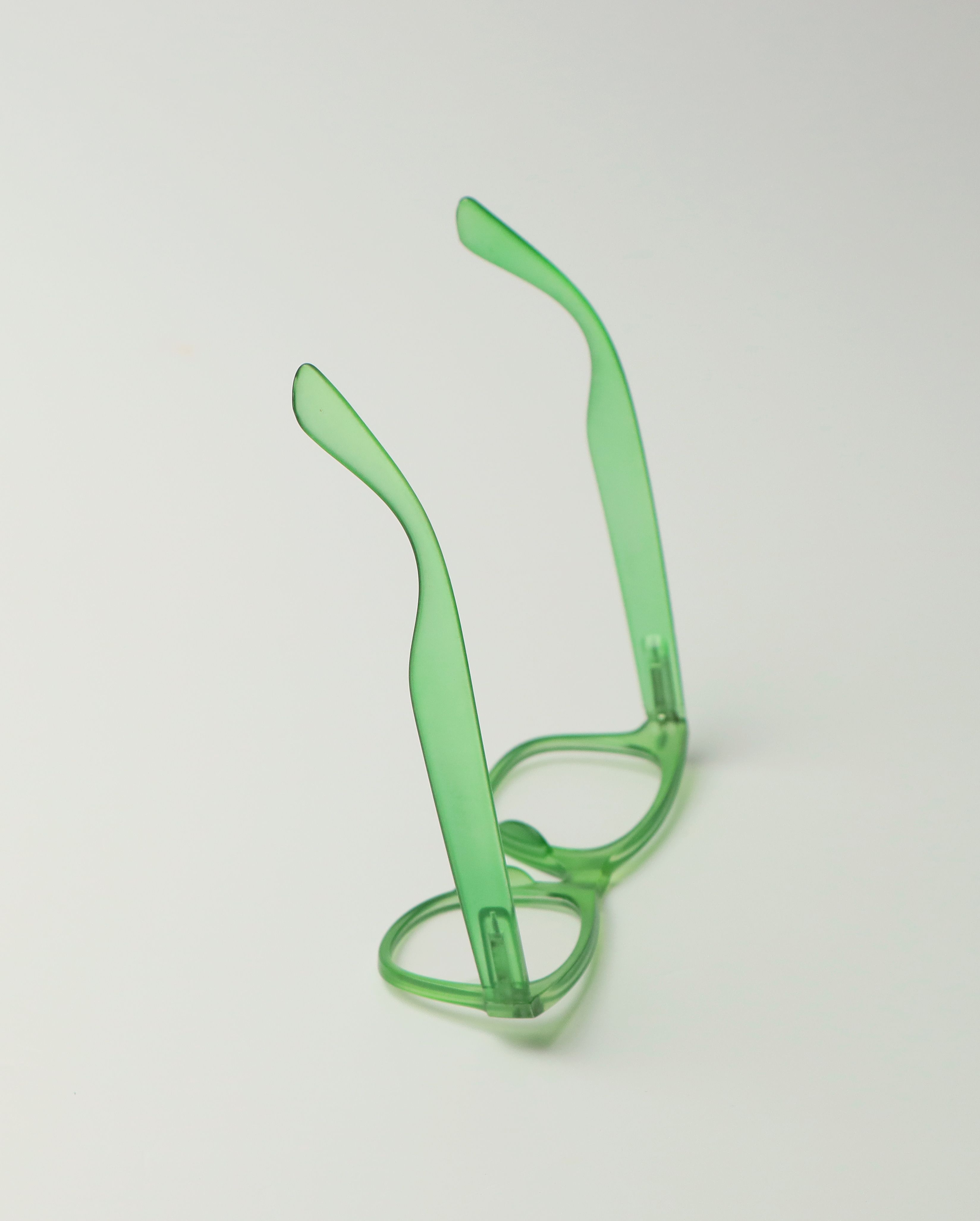 Minimalist green eyeglasses with a translucent design placed on a clean white surface.