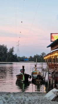 Tranquil view of traditional boats moored at sunset on a Thai river with colorful lights.