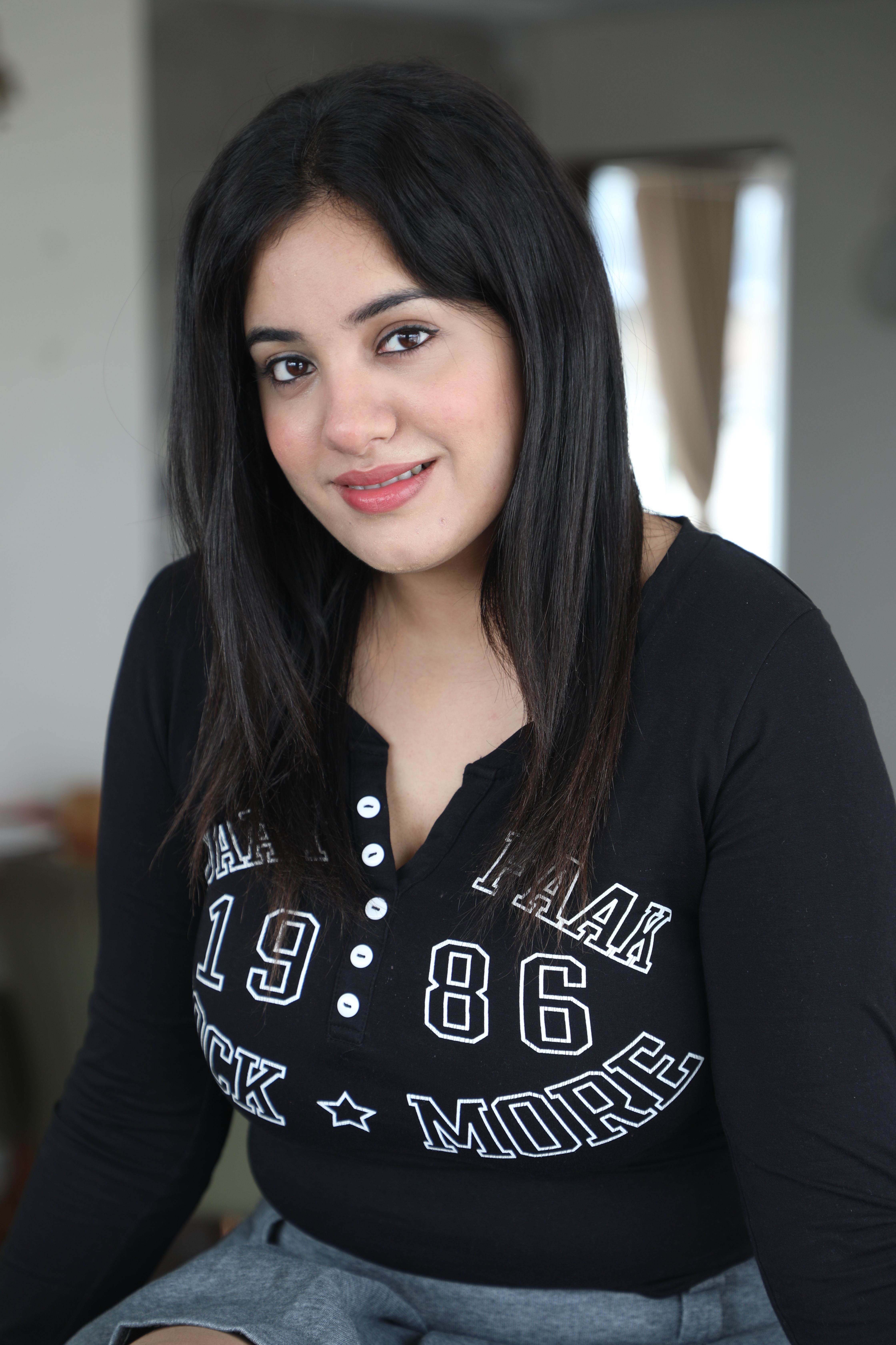 Young woman smiling confidently indoors with casual outfit in a cozy setting.