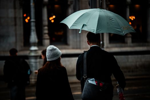 People walking under an umbrella in a moody, rainy Irish street scene.