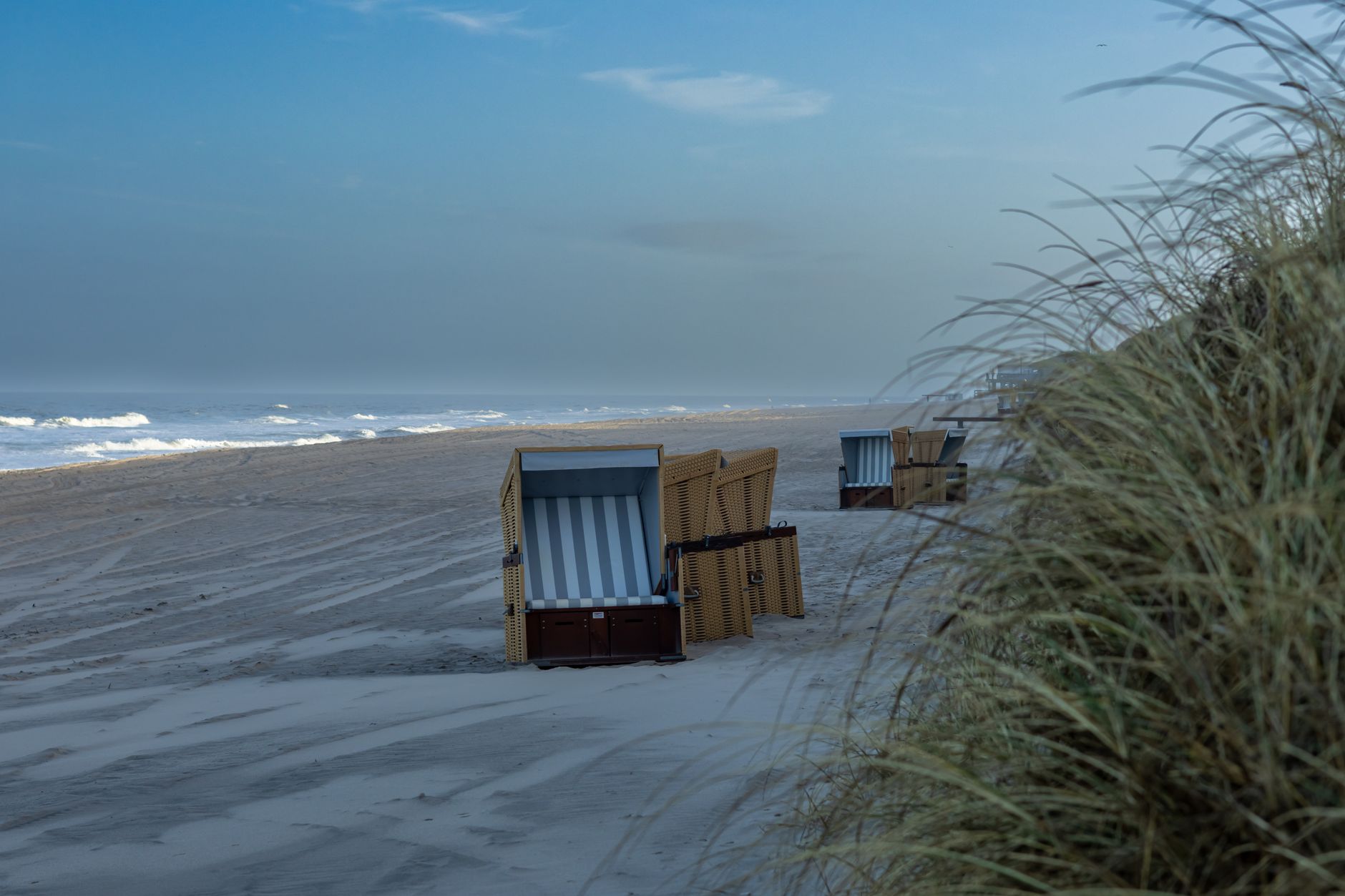 Peaceful beach scene with strandkorb chairs on the shoreline of Sylt Island, Germany, at daybreak.