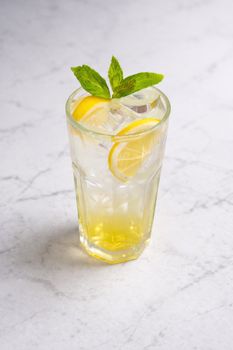 Tall glass of lemon mint iced drink on marble surface, perfect for summer refreshment.