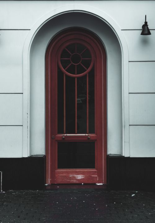Free A striking red arched doorway set within a classic white building facade, offering a blend of modern and vintage styles. Stock Photo