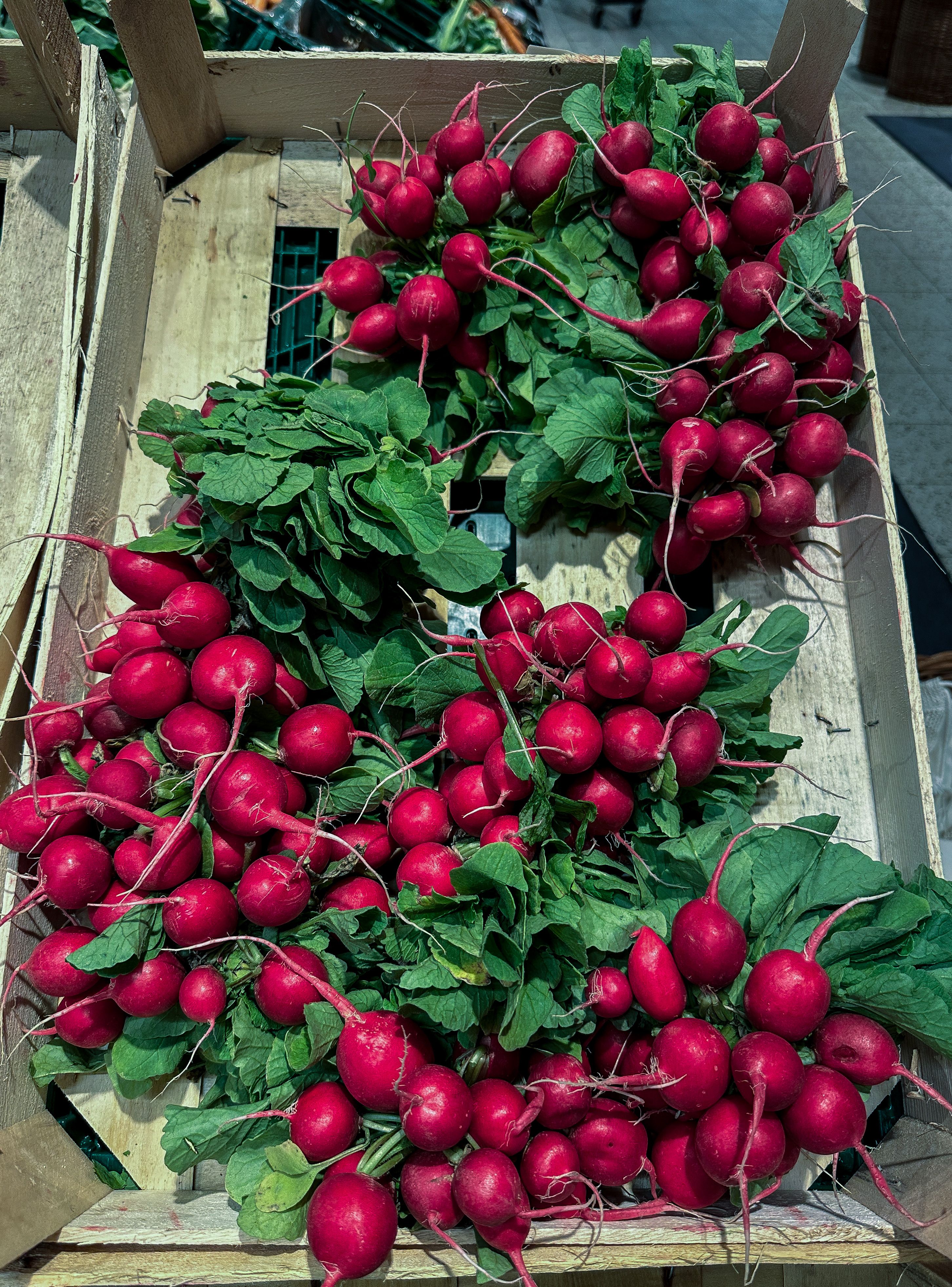 A vibrant display of fresh red radishes with green leaves in a wooden crate.