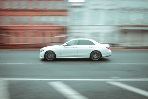 Free Dynamic side view of a white car speeding on a city street, motion blur effect. Stock Photo