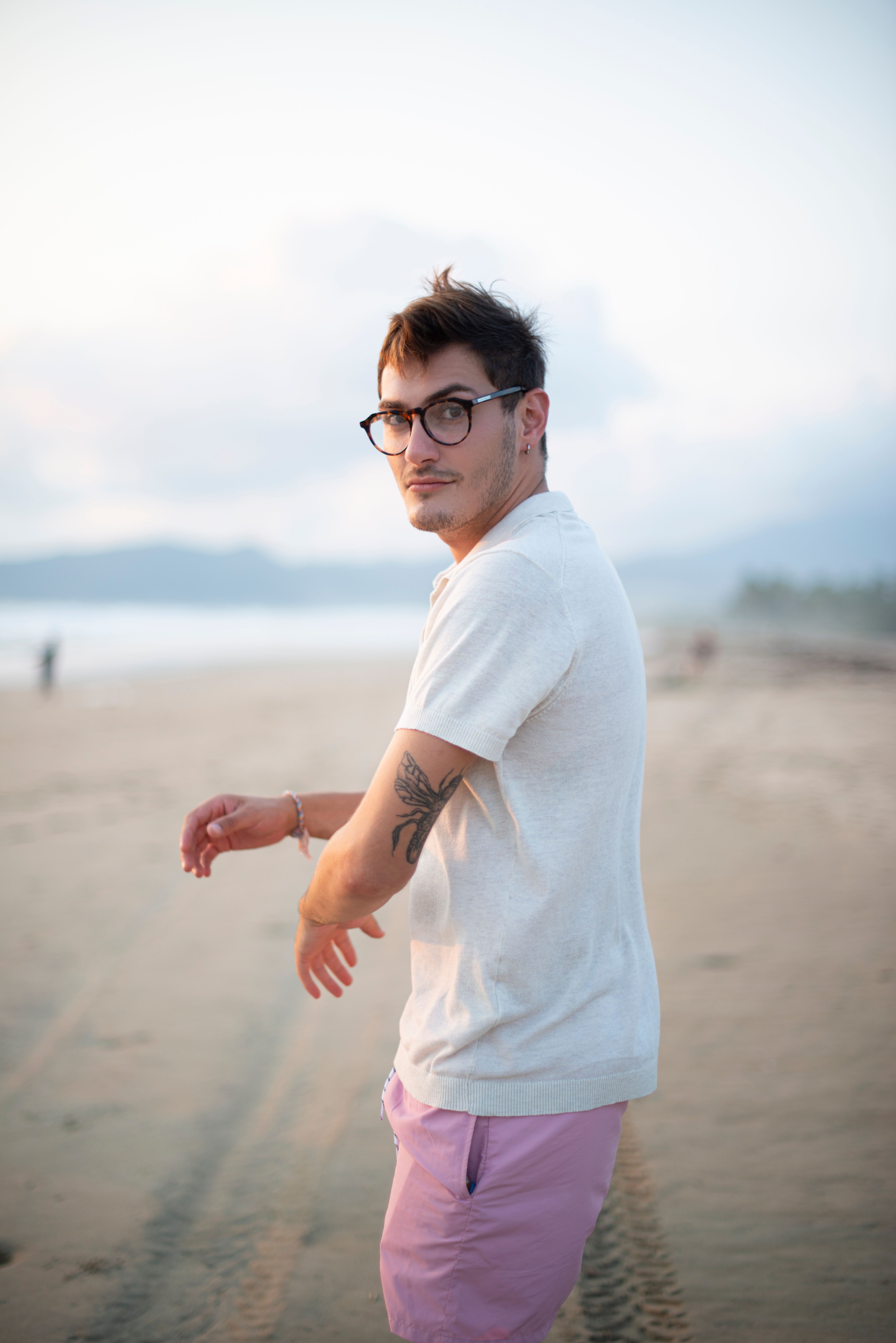 A young man walks along Playa Blanca, Mexico, wearing casual attire during a serene sunrise.