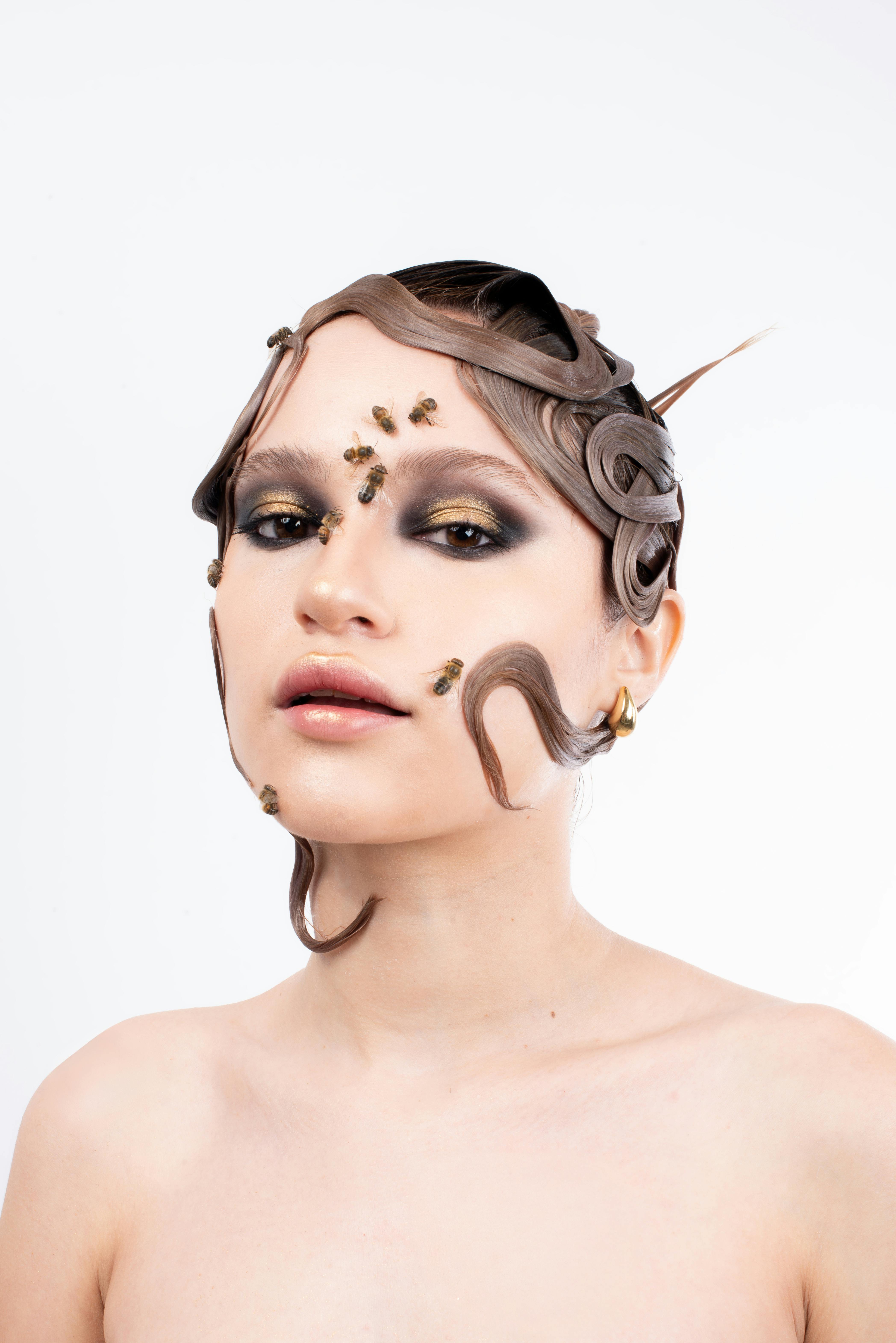 Striking fashion portrait with bees and artistic makeup against a white background.