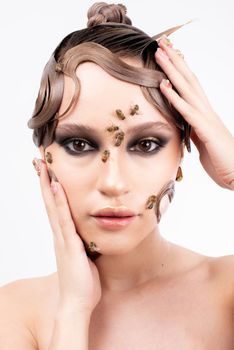 Creative makeup portrait featuring a woman with bees and unique hair styling on a white background.