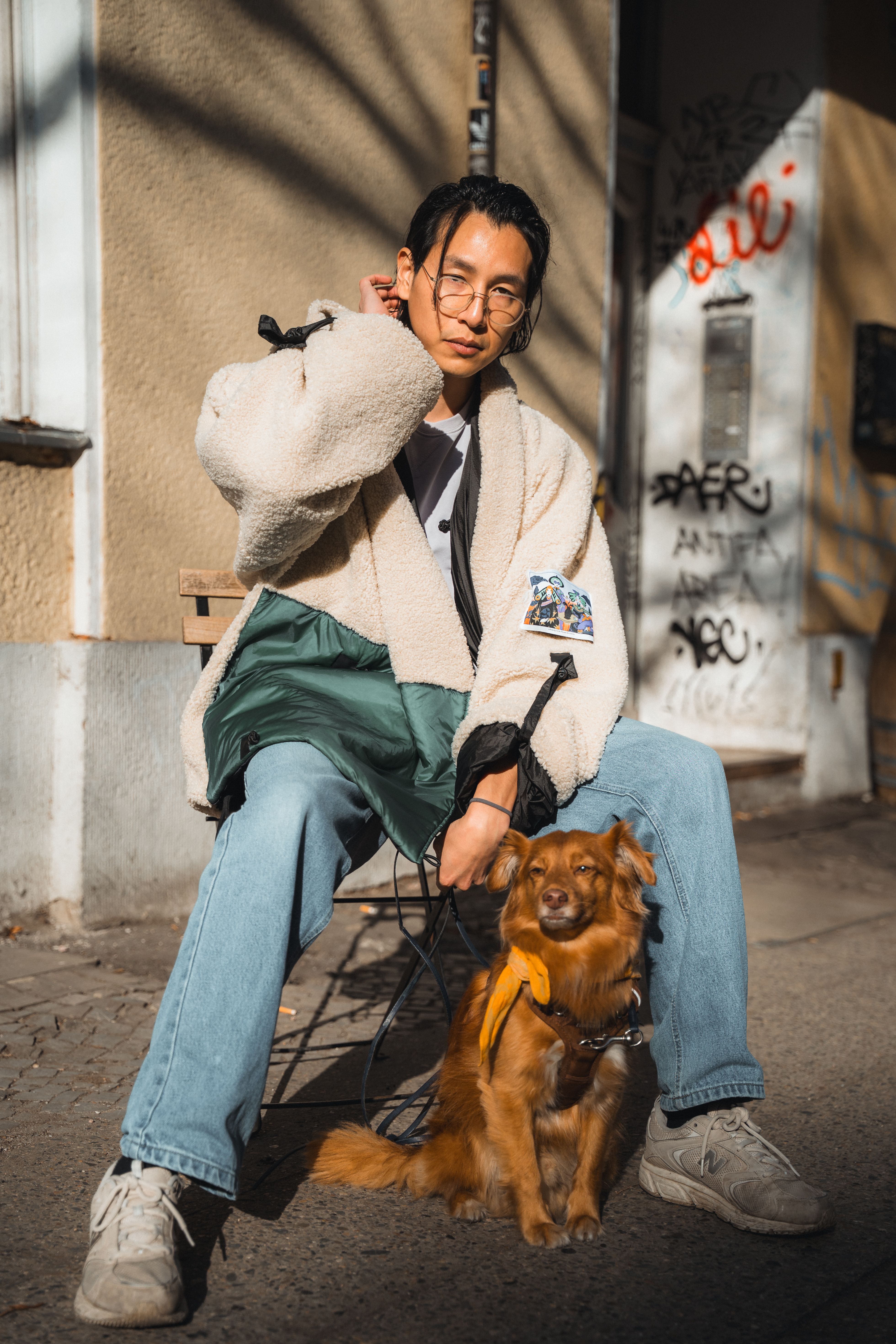 Stylish young man sits with a dog on a Berlin street, showcasing urban fashion and street art.