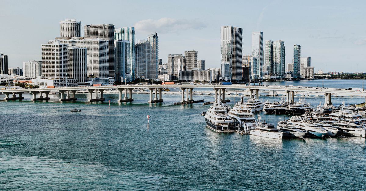 A scenic view of Miami skyline and marina, showcasing luxury yachts and modern skyscrapers under a clear blue sky.
