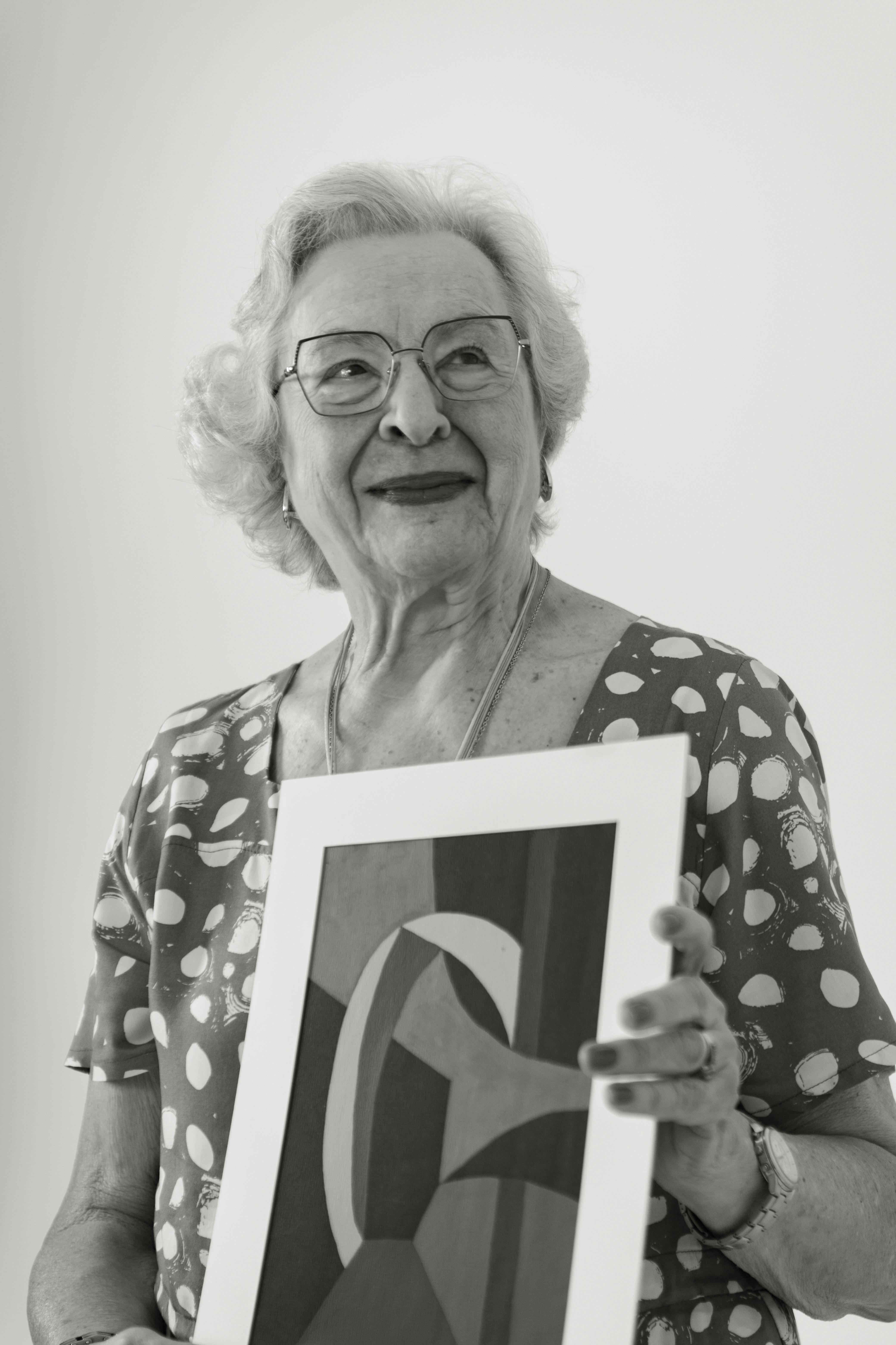 Senior woman in polka dot dress holding an abstract art print in black and white.