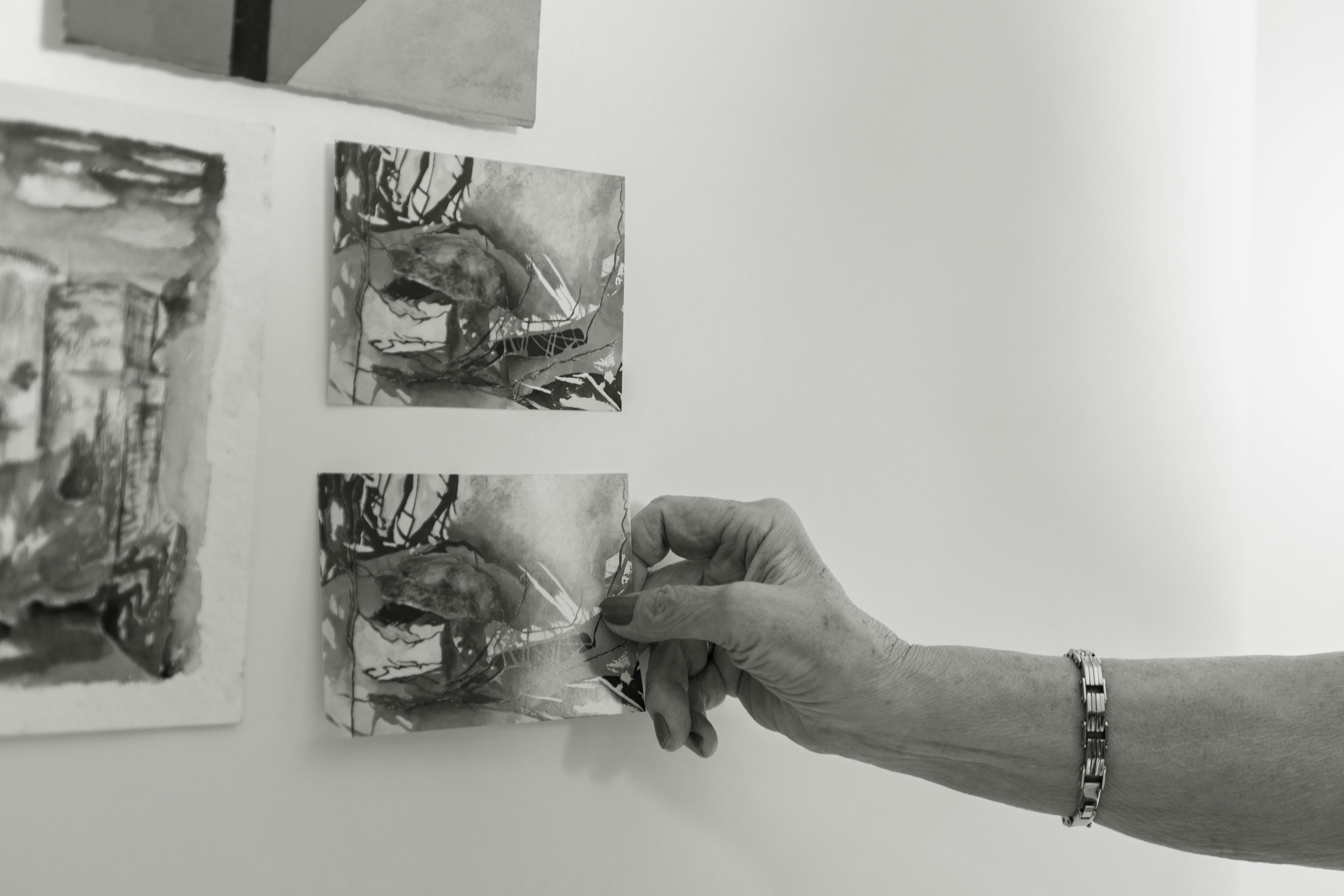A close-up of a hand arranging monochrome art prints on a wall in an artistic setting.