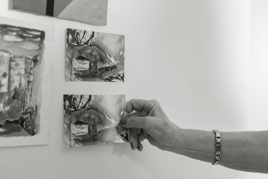 A close-up of a hand arranging monochrome art prints on a wall in an artistic setting. A close-up of a hand arranging monochrome art prints on a wall in an artistic setting.