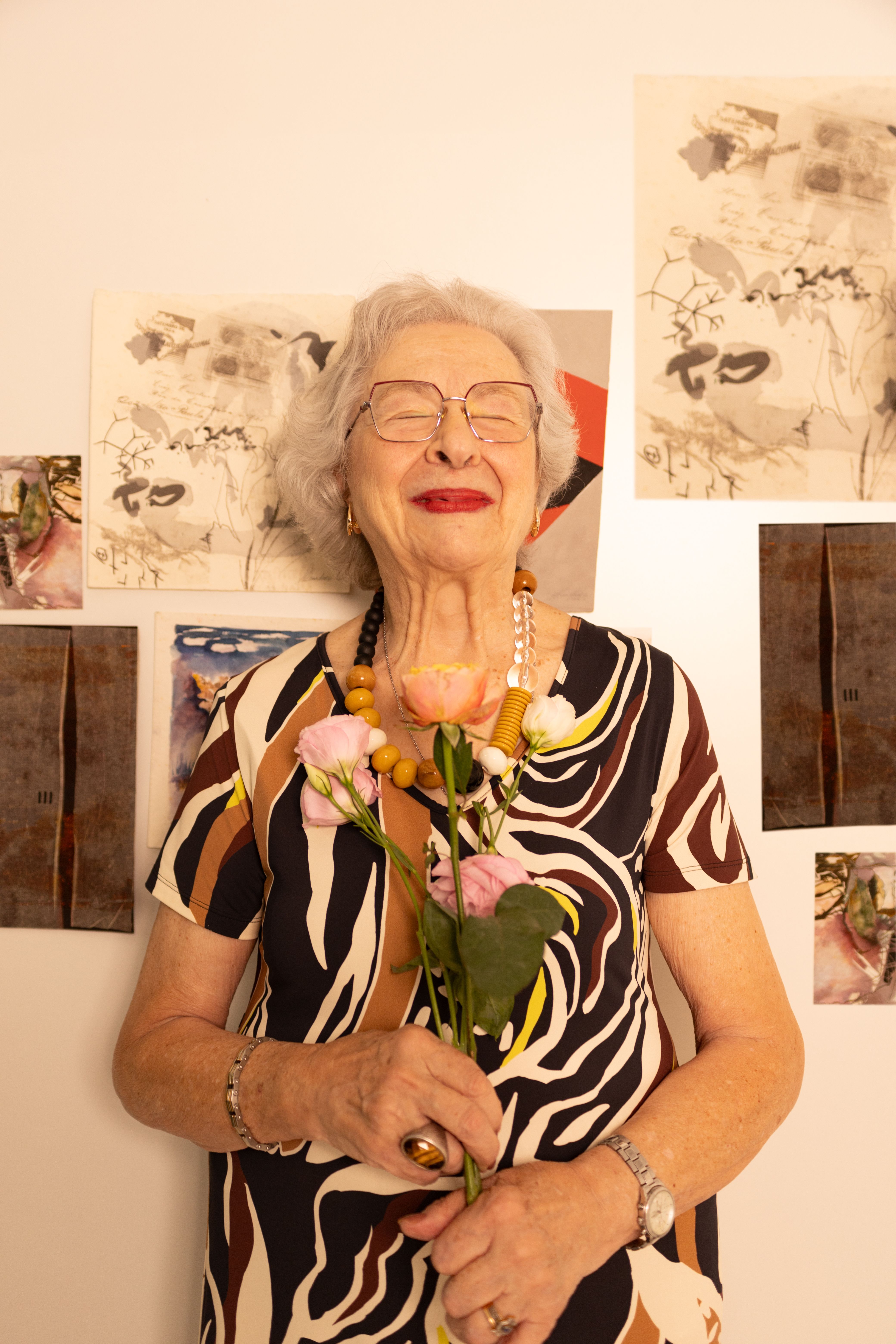 Joyful senior woman with flowers in vibrant dress indoors, smiling.