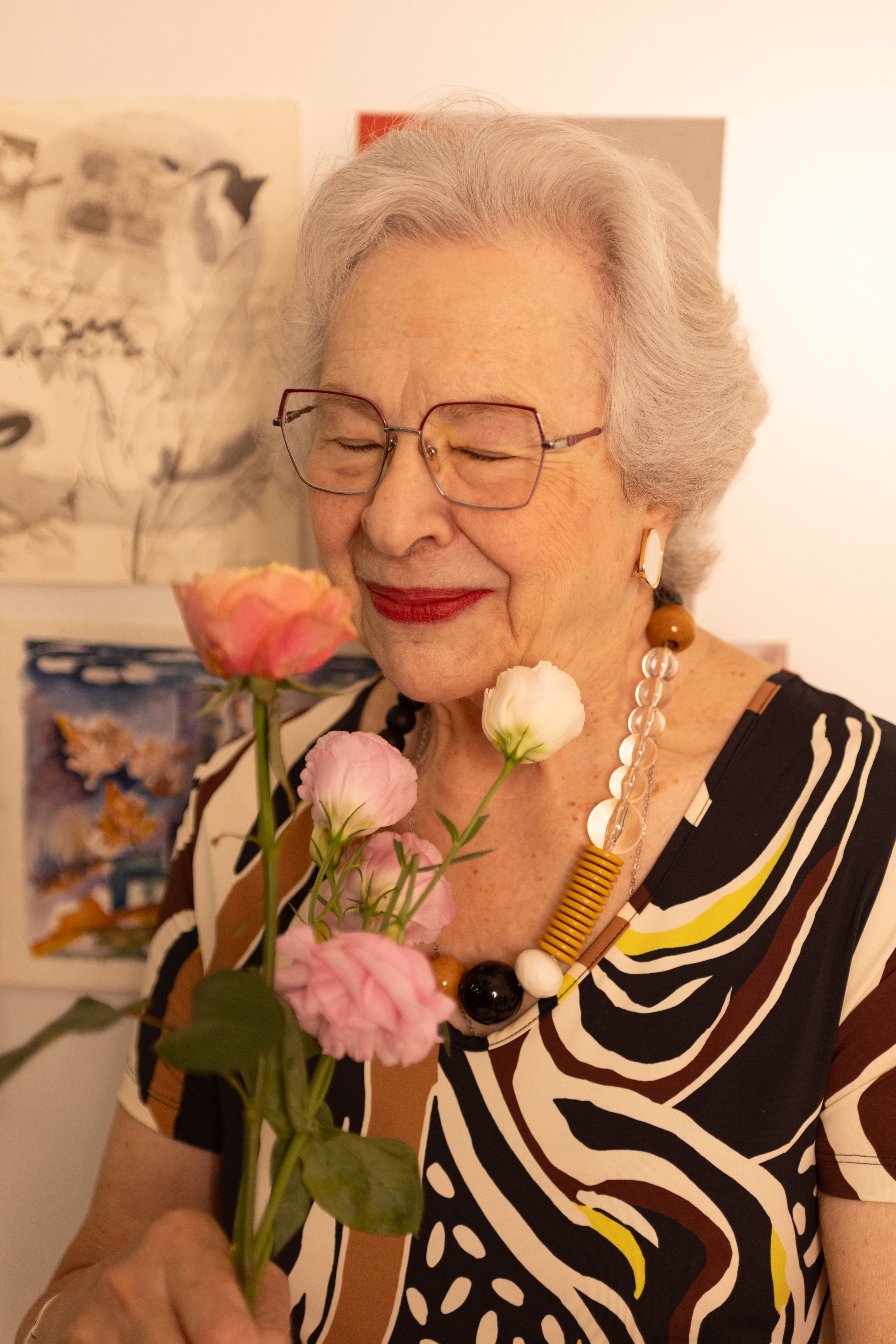 Senior woman smiling with flowers, radiating joy and elegance. Indoor setting with artistic backdrop.